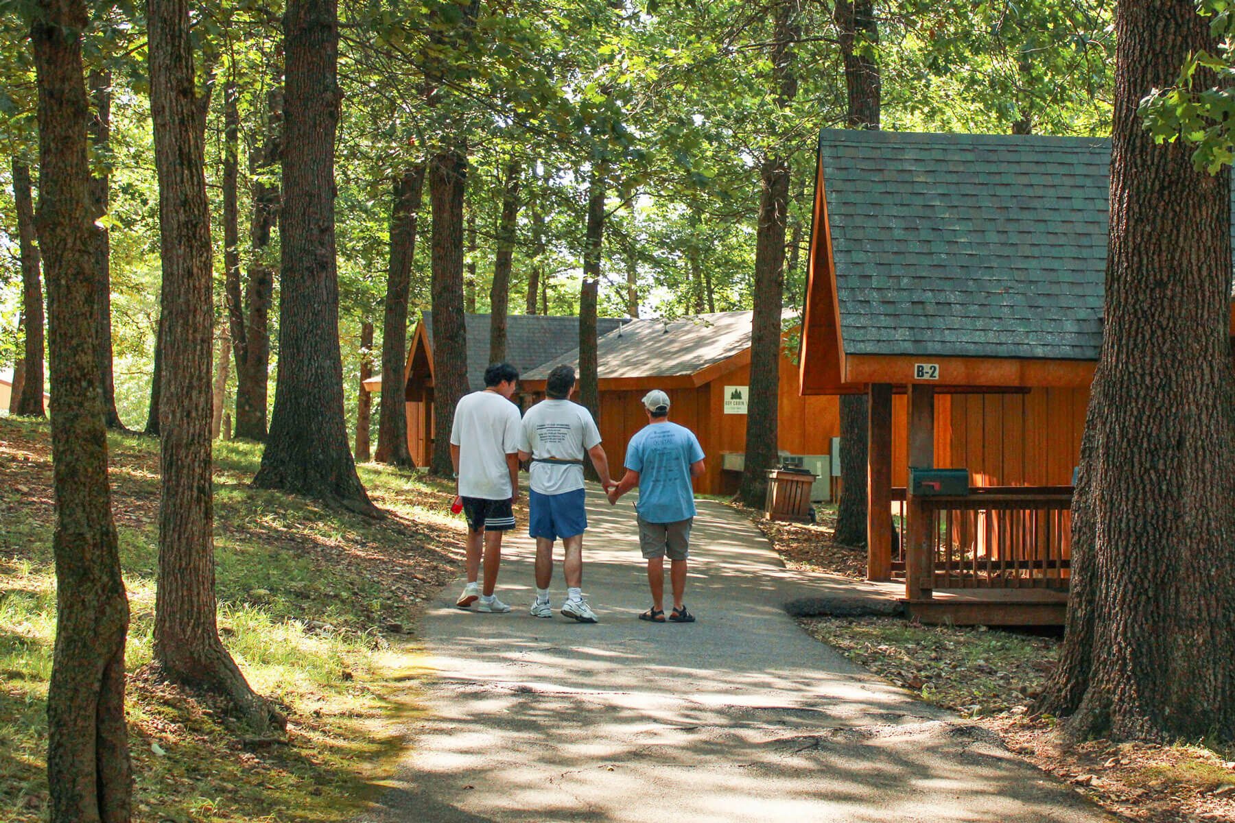 Campers walking on a path amid cabins, trees, and shadows