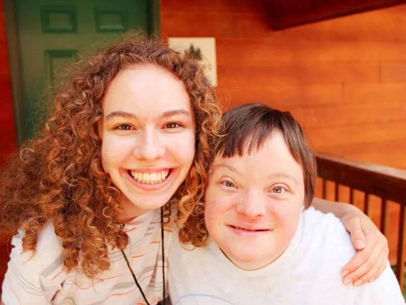 Camper and camp counselor smiling at the camera on a porch
